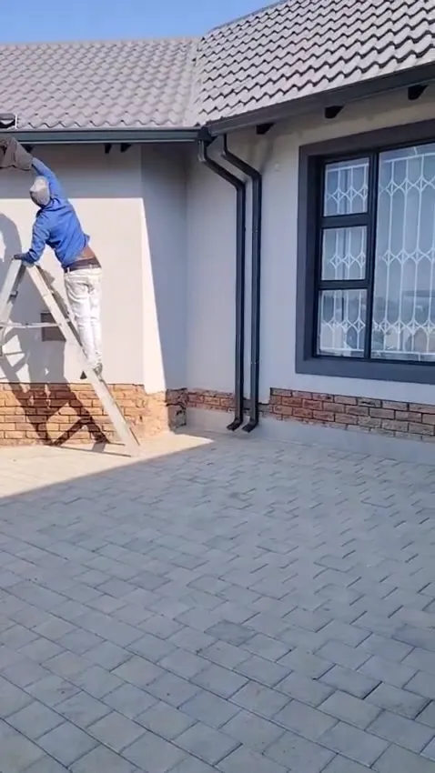 Elite Gutters installer on a ladder fitting a charcoal seamless gutter to a home